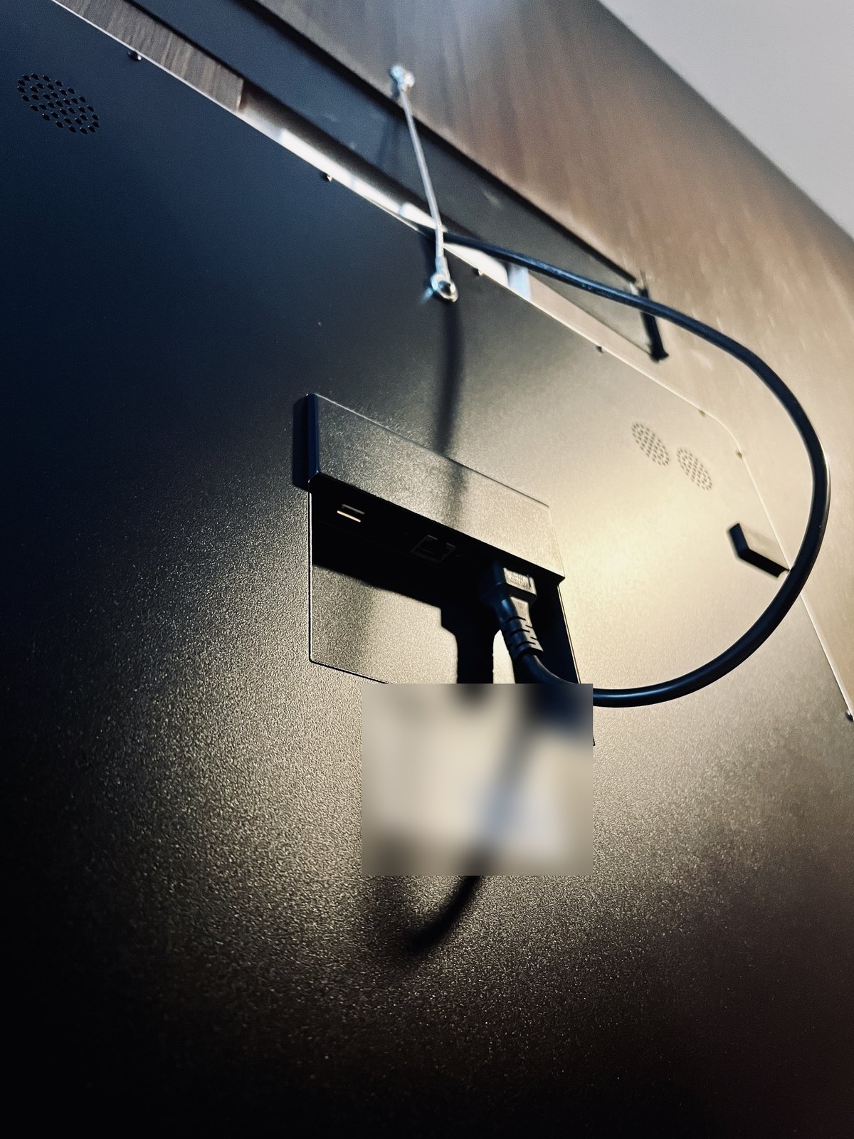 The back of the mirror, still hanging from its safety cable: a recessed panel with a USB port, an Ethernet jack, and the power lead, and two speaker grilles in the black casing